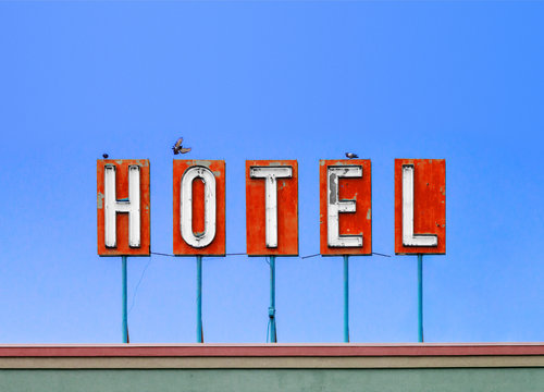 Red hotel sign on top of old motel isolated on blue sky background with birds