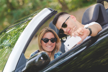 Beautiful couple taking self portrait from their cabriolet car in nature.