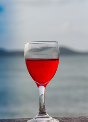 glass of red wine is placed on a wooden table. In the morning sea atmosphere of the summer.