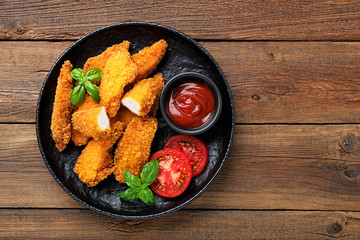 Delicious crispy fried breaded chicken breast strips with ketchup on black plate.