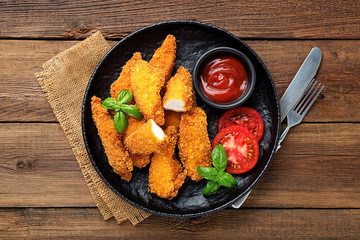 Delicious crispy fried breaded chicken breast strips with ketchup on black plate.