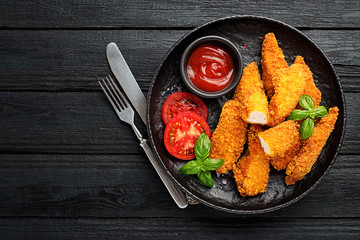 Delicious crispy fried breaded chicken breast strips with ketchup on black plate.