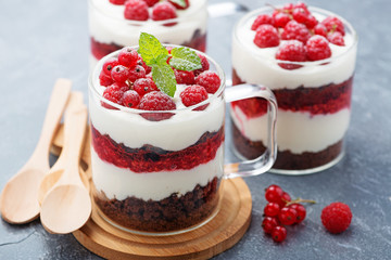 Layered dessert with raspberries,chocolate biscuit cake and cream cheese on a gray background.