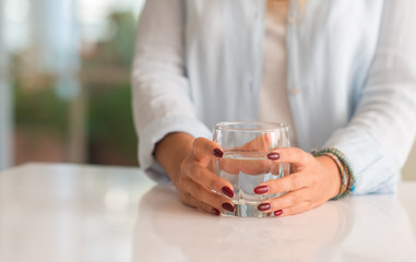 Fototapeta na wymiar Young woman hands holding a glass of water at home