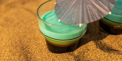 colorful shots drinks on a sandy beach with umbrellas for drinks