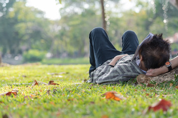 Middle age man laying down on the green grass sleeping and having book closed on his face in the evening.  Leisure on weekend.