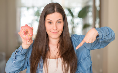 Hungry young woman holding pink donut with surprise face pointing finger to himself