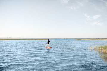 Man paddleboarding on the lake during the morning light, wide landscape view with blue water and sky