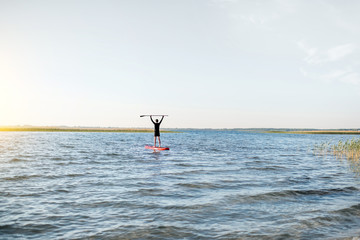 Fototapeta na wymiar Man paddleboarding on the lake during the morning light, wide landscape view with blue water and sky