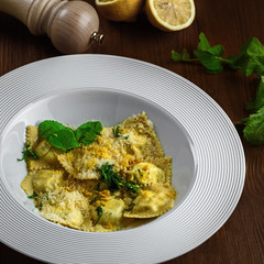 Tasty ravioli stuffed with ricotta, mint and grated lemon ring in a soup plate. First class Italian pasta food on a brown wooden table. Close-up shot.