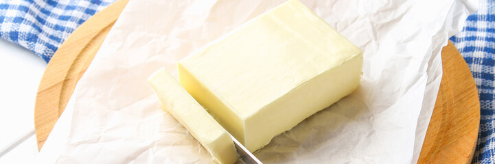 A bar of butter on a wooden board with a knife, on a white table. Ingredients for cooking.