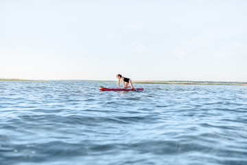 Beautiful young woman in black swimsuit paddleboarding on the lake with waves during the morning light