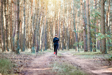 Fototapeta premium Woman in black sportswear running in the pine forest at the morning, wide landscape view