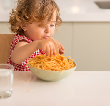 Beautiful blond child eating spaghetti with hands at home