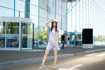 Young smiling traveler tourist woman in hat and light clothes standing at international airport. Female passenger traveling abroad to travel on weekends getaway. Air travel, flight journey concept.