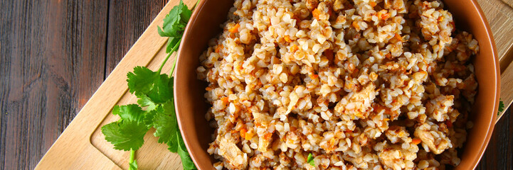 Boiled buckwheat in a bowl with pieces of chicken meat and cilantro on a brown wooden table.