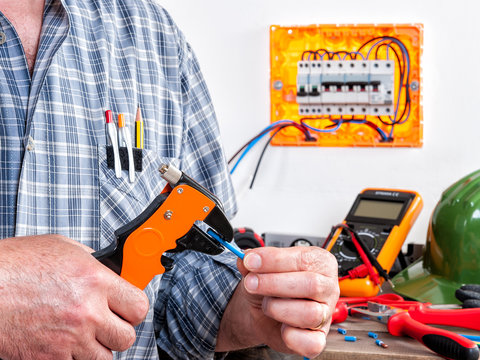 Electrician at work on cables with wire stripper.