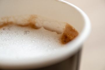 Close up of paper cup of hot coffee latte with milk foam on wooden table.