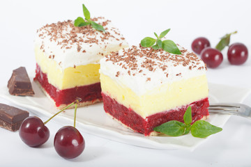 Sweet homemade cherry cake with vanilla and whipping cream on white plate. decorated with chuks of chocolates and mint leaves. Isolated on white background.