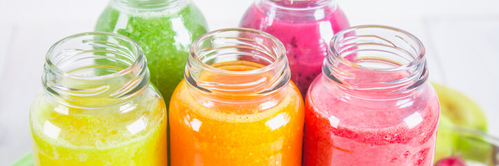 Multicolored smoothies in bottles of mango, orange, banana, celery, berries, on a wooden table.