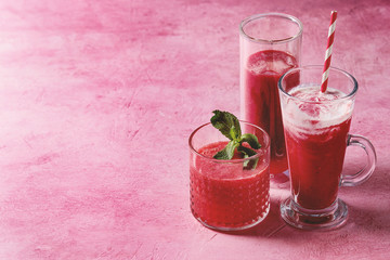 Three different red fruit berry watermelon, strawberry, raspberry, pomegranate cocktails or smoothies in glasses with fresh mint over pink background.