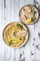 Homemade traditional spread hummus with pine nuts, olive oil, basil served on ceramic plate with pita bread over white wooden plank background. Flat lay, space. Mediterranean snack.