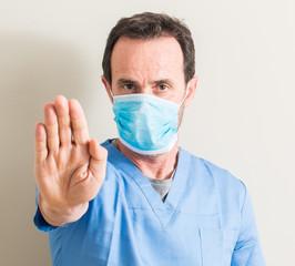 Senior doctor man using mask with open hand doing stop sign with serious and confident expression, defense gesture
