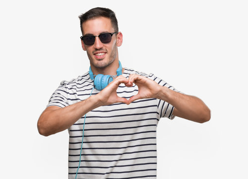 Handsome young man wearing headphones smiling in love showing heart symbol and shape with hands. Romantic concept.