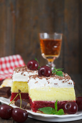 Homemade cherry cake with vanilla and whipping cream on wooden table. Glass of and cherry brandy in backround.Vertical image.