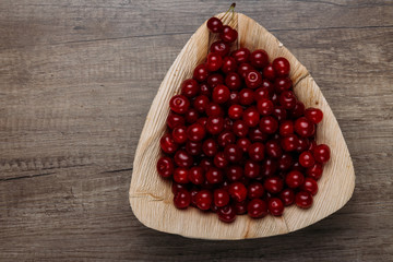 fresh red cherries in a wooden plate on a wooden table. wooden plate on a wooden background. a plate in the form of a triangle. ecology. proper nutrition.
