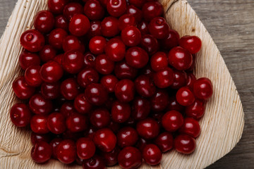 fresh red cherries in a wooden plate on a wooden table. wooden plate on a wooden background. a plate in the form of a triangle. ecology. proper nutrition.