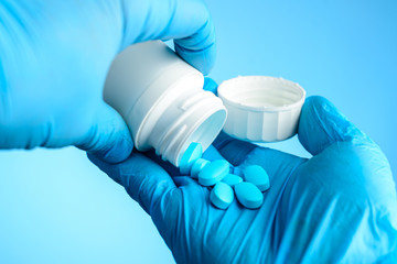 Unknown doctor pours the blue pills out of the bottle into hands