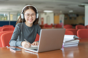 Beautiful smiling female student using online education service. Young woman looking in laptop display watching training course and listening it with headphones. Modern study technology concept