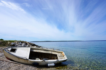 Fototapeta na wymiar Seacoast with pebble beach and old, damage, rust, fisherman boat sunk on the beach in the blue lagoon