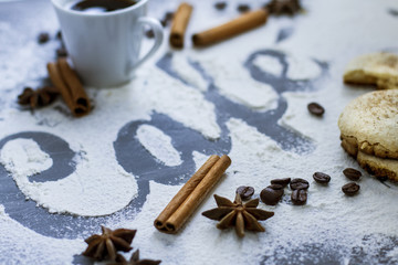 Obraz na płótnie Canvas Dark table decorated with the word coffee made from wheat flour, plus a cup of fresh coffee and cinnamon stick with star anise and biscuits
