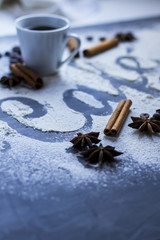 Dark table decorated with the word coffee made from wheat flour, plus a cup of fresh coffee and cinnamon stick with star anise