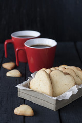 Tasty homemade gingerbread and coffee in two red cups on a black wooden background.