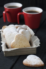 Tasty homemade gingerbread and coffee in two red cups on a black wooden background.