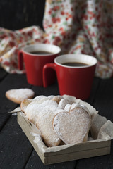 Tasty homemade gingerbread with powder and coffee in two red cups on a black wooden background.