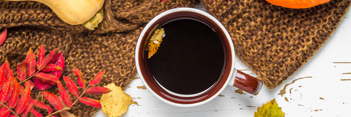 Mug of hot coffee in autumn setting on a wooden table with a knitted scarf, sweater. Comfort, warmth, cozy. banner