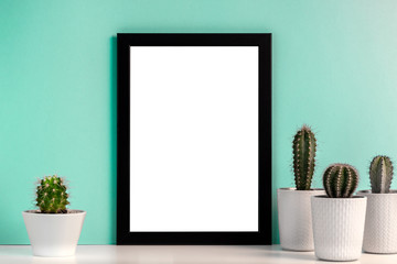 Fototapeta premium Empty mockup frame with groupe of cactuses on the background of the mint wall