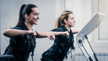Young athletic women in EMS suits exercising in modern gym - obrazy, fototapety, plakaty