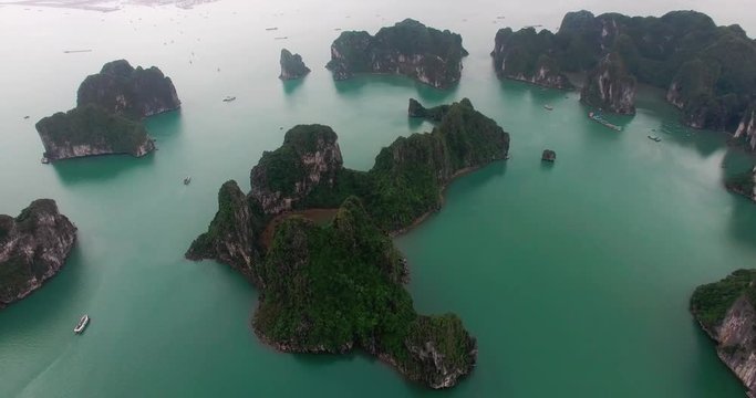 Halong Bay, Vietnam, high above aerial view, panning left over islands and boats, town in the background, cloudy morning, drone view.