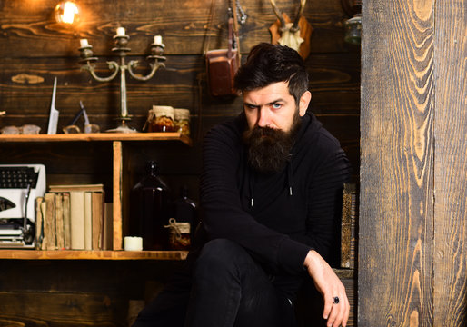 Spending great time at home. Man with beard looks strictly. Man bearded enjoy evening, wooden background. Guy in cozy warm atmosphere relaxing but looks tense