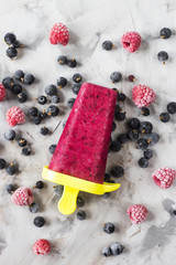 Berry ice cream on a stick of raspberries and currants, homemade with the help of special molds. On a gray table among frozen berries. Top view, flat lay
