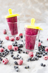 Berry ice cream on a stick in transparent glasses. Homemade of raspberries and currants, cooked with special forms. On a gray table among frozen berries