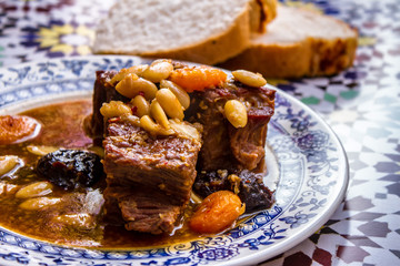 Moroccan beef, prunes and almonds tagine. Stewed meat on a plate with blue ornament. Recipe cookbook background