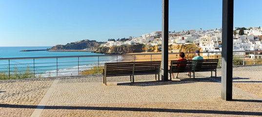 Dos turistas mayores sentados en un banco en la playa de Albufeira, una de las más visitadas por...