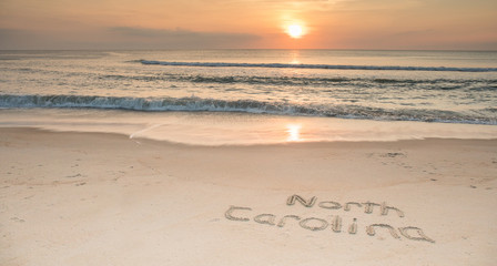 Fototapeta na wymiar The words North Carolina etched in the sand at sunrise with waves coming ashore.