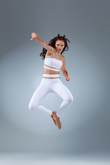 Attractive excited fitness girl, ballerina dancer in sportwear jumping of joy isolated over gray background.